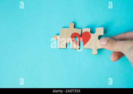 Female hand connecting puzzle with drawn red heart on blue background. Love concept. St. Valentine day. Reconciliation. Reunion concept. Copy space. Stock Photo