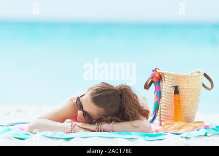 relaxed stylish 40 year old woman with long curly hair in elegant black swimsuit on a white beach sleeping. Stock Photo