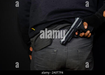 asian man holds a gun. Gun in his hand from the back isolated on black background. Stock Photo