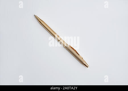 Gold writing ball point pen with detailed textures laying diagonally isolated on a light background. Stock Photo