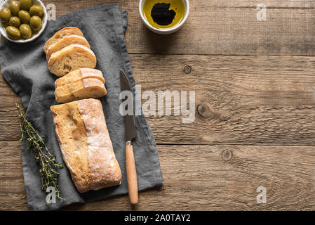 Ciabatta. Fresh italian ciabatta bread with herbs, olive oil and olives on wooden background, top view, copy space. Stock Photo