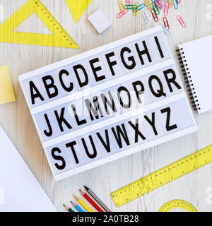 Back to school concept. Letters from A to Z. English alphabet on a lightbox and accessories for study on a white wooden background, top view. From abo Stock Photo