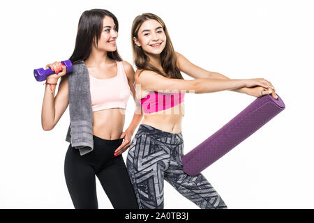 Sporty woman lifts heavy dumbbell, works on muscles, wears headband, casual purple t shirt, cheerful girl holds fitness mat. Stock Photo