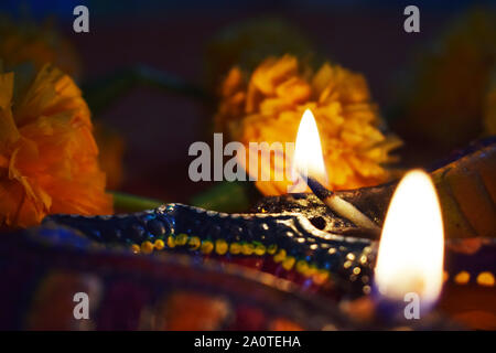 Pair of colorful Diyas lit for Happy Diwali with selective focus on glow and marigold flower as background Stock Photo