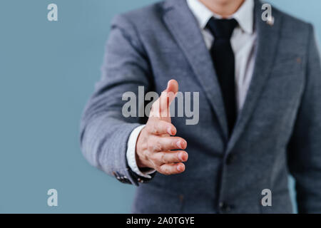 Businessman in suit extending hand, ready for handshake over blue background Stock Photo