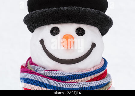 Portrait of a smiling snowman with a striped scarf and a black hat. Button eyes and carrot nose Stock Photo