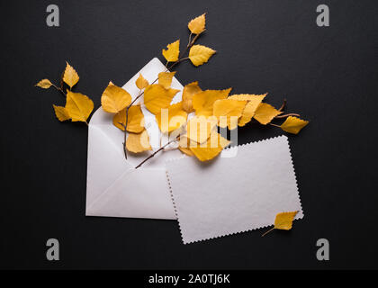Autumn card with yellow foliage on a black background. Envelope with a white blank sheet of paper. Place for promo or greetings text Stock Photo