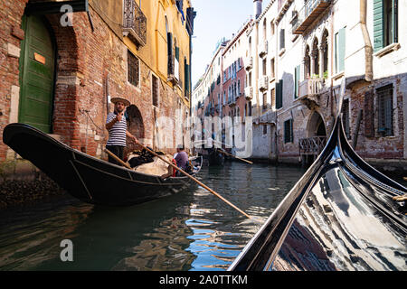 A gondolier in a traditional striped shirt and straw boater hat on a gondola on the canals of Venice, Italy. Wearing modern mirror sunglasses. Stock Photo