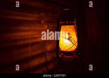Spooky old retro kerosene lantern lamp with light cast on corrugated iron wall and dark black background Stock Photo