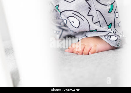 Close up of baby's feet while standing up in the crib. Wearing a cute pair of pants in a bright minimalistic modern nursery bedroom. Stock Photo