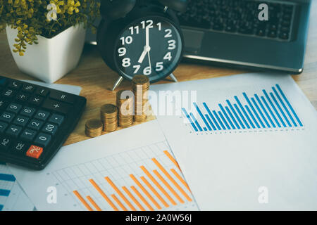 Coin stack and financial graph paper sheet with notebook calculator and alarm clock on working table, business finance concept idea. Stock Photo