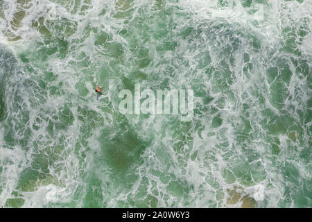 Straight down shot of man swimming in breaking waves with wite water everywhere.