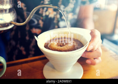 A barista makes coffee drip. Hand Drip Coffee, Barista pouring hot water on the roasted coffee ground with filter. Drip coffee brewing. Stock Photo
