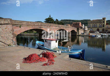 fishing net and a fishing boat on the pier on the Temo river of Bosa town in the northern Sardinia. An old bridge in the background Stock Photo