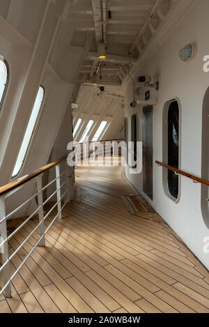 Windows of enclosed forward section of the Queen Mary 2's promenade deck cast attractive shadows, the spare propellor blades on the forecastle outside Stock Photo