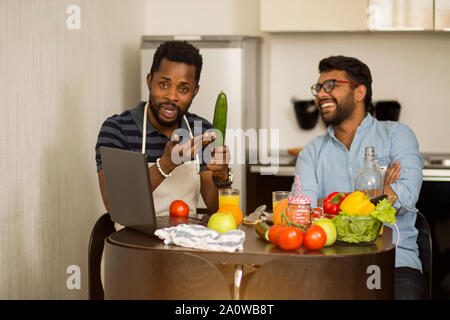 Handsome amazed african american young man pointing with finger to his indian friend who going to cook and smiling. Joyful multi ethnic students sitti Stock Photo