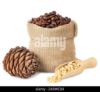 unpeeled cedar nuts in burlap sack with heap of kernels in wooden scoop and pine cone isolated on white background Stock Photo