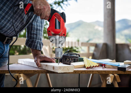 Adult craftsman carpenter with electric drill works makes a hole on a wooden table. Housework do it yourself. Stock photography. Stock Photo