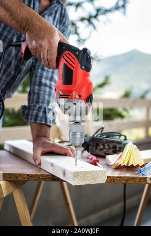 Adult craftsman carpenter with electric drill works makes a hole on a wooden table. Housework do it yourself. Stock photography. Stock Photo