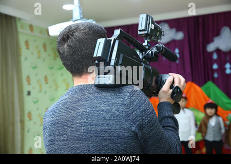 Video camera operator working with his equipment - Image . Video Camera recording kindergarder room with blurred background . Stock Photo