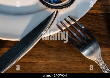 Artistic view of the fork, spoon and knife on a plate. Conceptual image about danger of eating too much tasty food. Stock Photo