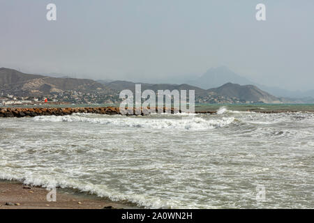 red flag on the breakwater of the beach after the storm, with the mountain coast in the background Stock Photo