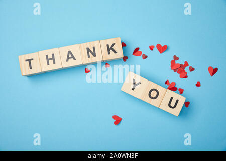 top view of wooden cubes with thank you words and red paper hearts on blue background Stock Photo
