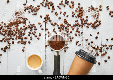 Top view of paper cup between portafilter and cup of espresso on white wooden surface with coffee beans Stock Photo