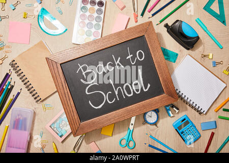 top view of various school supplies and chalkboard with back to school lettering on wooden desk Stock Photo