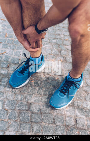 cropped shot of sportsman in sneakers touching injured leg Stock Photo