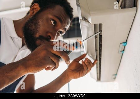 serious african american repairman fixing air conditioner with screwdriver Stock Photo