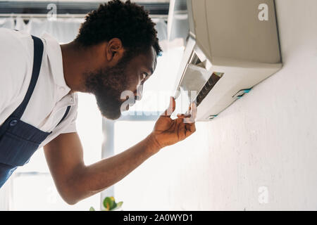 concentrated african american repairman looking at broken air conditioner Stock Photo