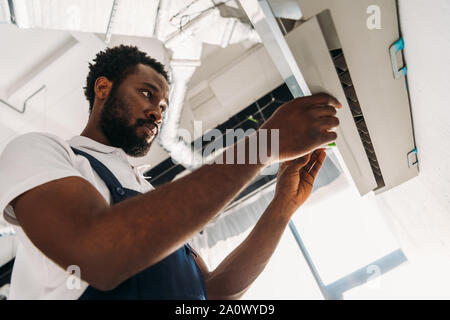 concentrated african american repairman standing on ladder and fixing air conditioner Stock Photo