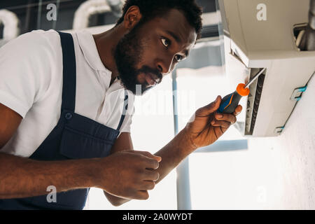 attentive african american repairman fixing air conditioner with screwdriver Stock Photo