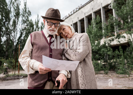 PRIPYAT, UKRAINE - AUGUST 15, 2019: elderly couple looking at photo near building in chernobyl Stock Photo