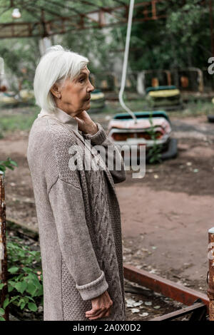 senior woman standing in amusement park near abandoned bumper cars Stock Photo