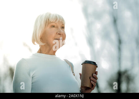 Joyful comely senior lady holding coffee to go in hand Stock Photo