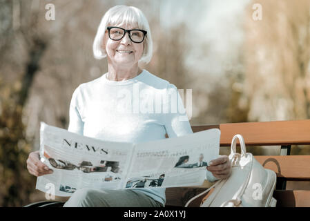 Beaming elegant elderly missis holding paper in the park Stock Photo