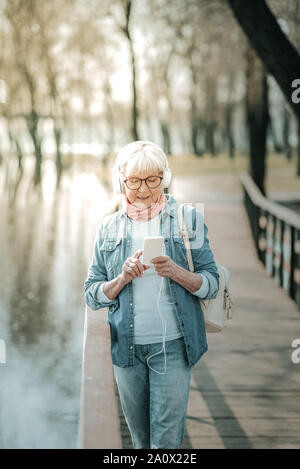 Concentrated elderly missis wearing headsets switching music on the player Stock Photo