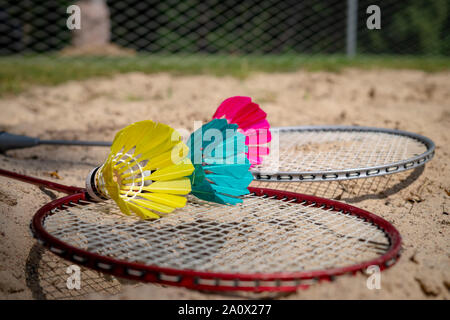 Colorful feathered shuttlecocks in blue, yellow and pink with a badminton net and racket Stock Photo