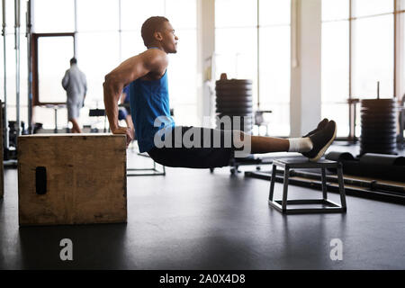 Side view portrait of muscular African-American man doing pull ups on plywood box during cross training in gym, copy space Stock Photo