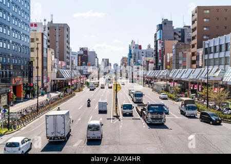 Main route, street through Sugamo town in Tokyo, Japan. View along street busy with traffic from overhead bridge. Buildings on either side. Stock Photo