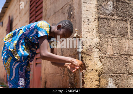 African Woman Washing Hands under Tap Outdoors Stock Photo