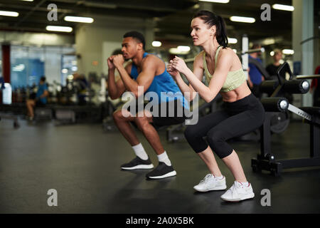 Side view portrait of sportive couple doing squats during fitness workout in modern gym, copy space Stock Photo