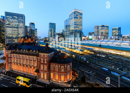 Tokyo. High angle view of the Marunouchi side of the red brick Tokyo station building with station platforms and High rise blocks behind. Night time. Stock Photo