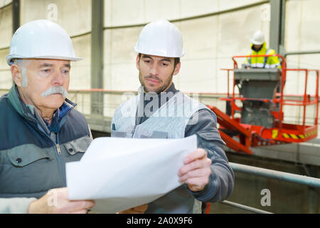 senior engineer and colleague in hardhat standing in factory Stock Photo