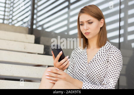 Upset stressed woman holding cellphone frustrated with the message she received. Negative emotion, face expression. Girl sitting outdoors near her off