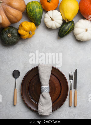Autumnal serving plate with decoration as green, yellow, white and orange pumpkins on gray concrete. Wooden tableware with napkin at empty plate. Conc Stock Photo