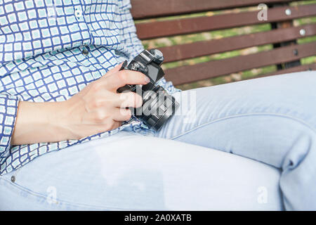 Antique camera in the hands of a girl in blue jeans and a blue shirt. On a park bench. Preparing for a photo shoot Stock Photo