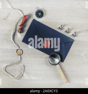 Blank black envelope and vintage stationery: wax seal, stamp, magnifier and compass on light wood table background. Mockup for your design. Stock Photo
